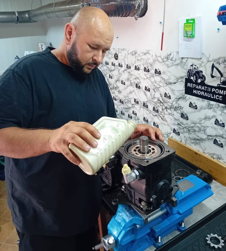 Constantin completează uleiul unei pompe hidraulice în atelier